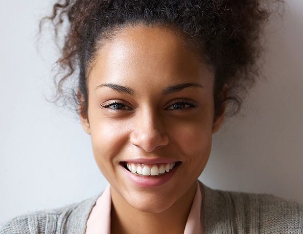 Junge Frau mit braunen, lockigen Haaren. Sie trägt einne grauen Cardigan und eine rosa Bluse.